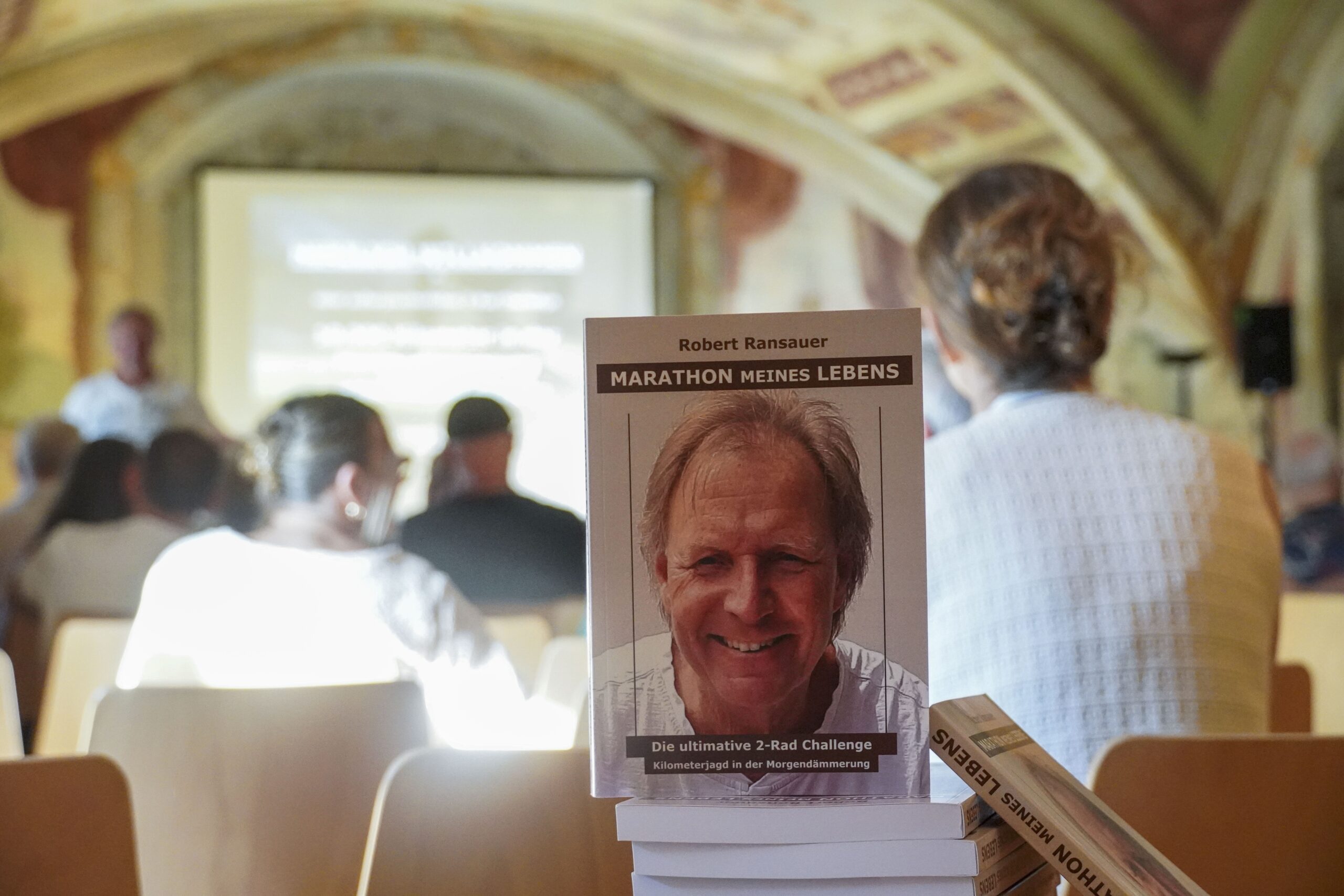 Robert Ransauer mit seinem Buch "Marathon meines Lebens" vor Publikum in einem Saal